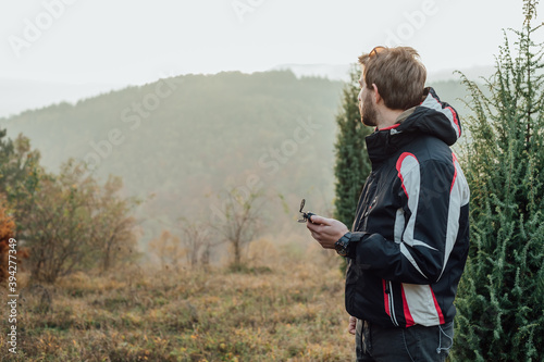 A young man uses a military compass for orientation in nature, talking on the phone, surrounded by fog.