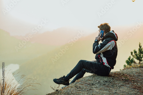 A young man uses a military compass for orientation in nature, talking on the phone, surrounded by fog.