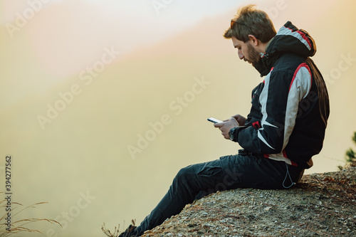A young man uses a military compass for orientation in nature, talking on the phone, surrounded by fog.
