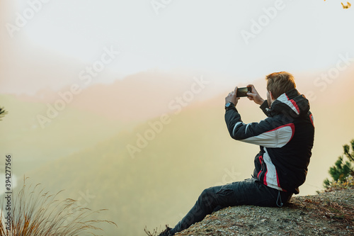 A young man uses a military compass for orientation in nature, talking on the phone, surrounded by fog.