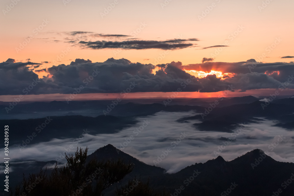 Mount Warning, New South Wales, Australia: Beautiful sunrise view from the mountain top. Storm clouds hiding the sun and dense clouds in the valleys of the volcano crater. Background image.