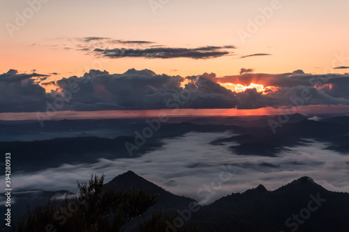 Mount Warning, New South Wales, Australia: Beautiful sunrise view from the mountain top. Storm clouds hiding the sun and dense clouds in the valleys of the volcano crater. Background image.
