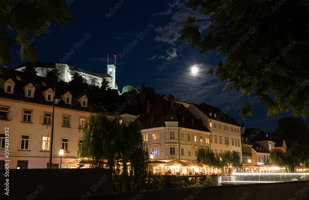 Ljubiljana, Slovenia: Image of the promenade during night with the moon shining on the castle.