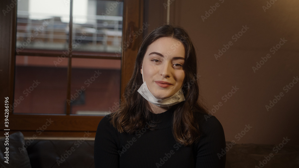 Young girl sitting on the sofa and she take off the mask looking at the camera and smiling, lifestyle and pandemic concept Young girl sitting on the sofa and she take off the mask looking at the camera and smiling, lifestyle and pandemic concept