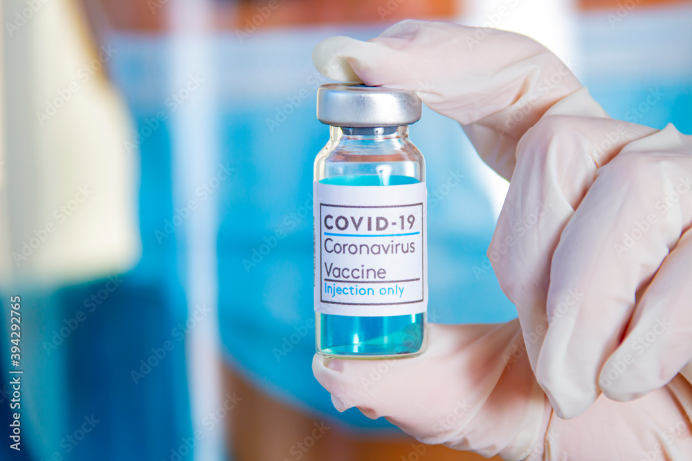 A health worker holding a bottle of Covid-19, Coronavirus or SARS-CoV-2 vaccine on a Sterile Transparent Vial with a white and blue label a white globes A health worker holding a bottle of Covid-19, Coronavirus or SARS-CoV-2 vaccine on a Sterile Transparent Vial with a white and blue label a white globes