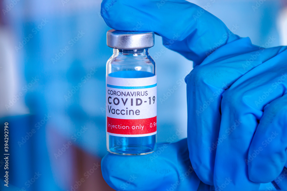 A health worker holding a bottle of Covid-19, Coronavirus or SARS-CoV-2 vaccine on a Sterile Transparent Vial with a red, white and blue label and blue globes. A health worker holding a bottle of Covid-19, Coronavirus or SARS-CoV-2 vaccine on a Sterile Transparent Vial with a red, white and blue label and blue globes.