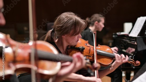 Focus on a young woman playing the violin with a string quartet and grand piano. Selective focus