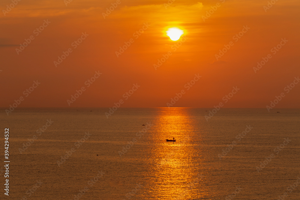 日の出の太陽の光を浴びる小舟と漁師