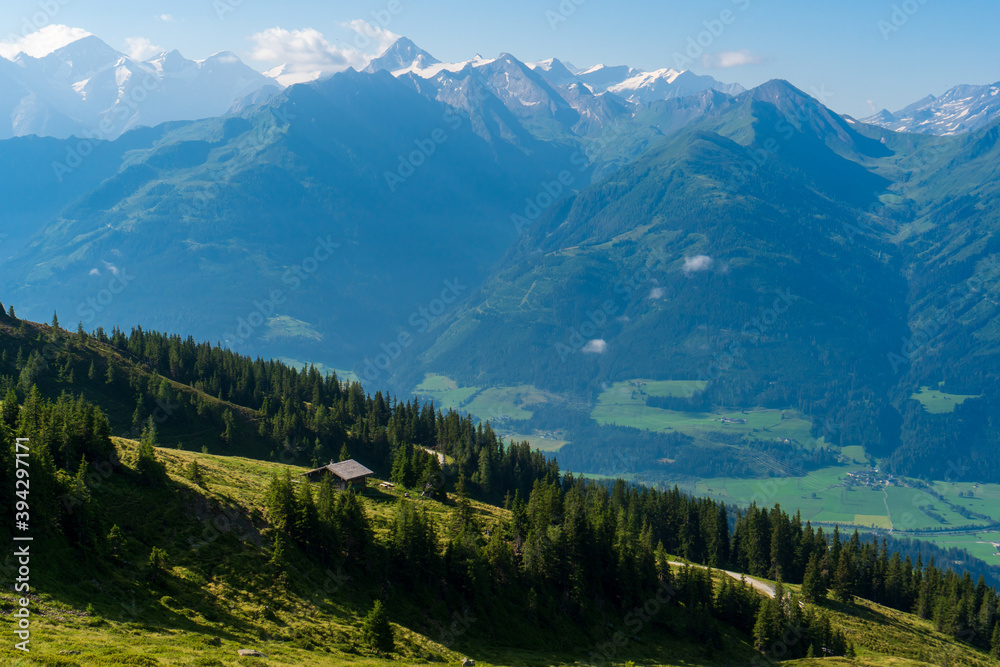 Scenic summer view on snowy grossglockner peak and nordlicher bockkarkees in sunny day with green meadows, pine tree forests, hills, blue sky. Europe alps in austria