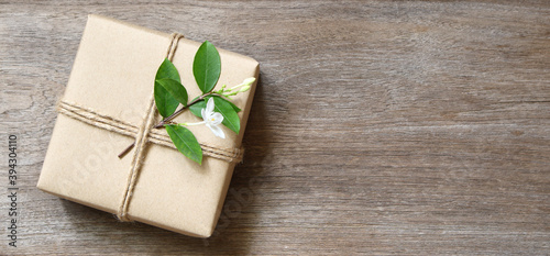 gift box wrapped in recycled paper with rope and leaf on wood background with copy space for text or image / green concept