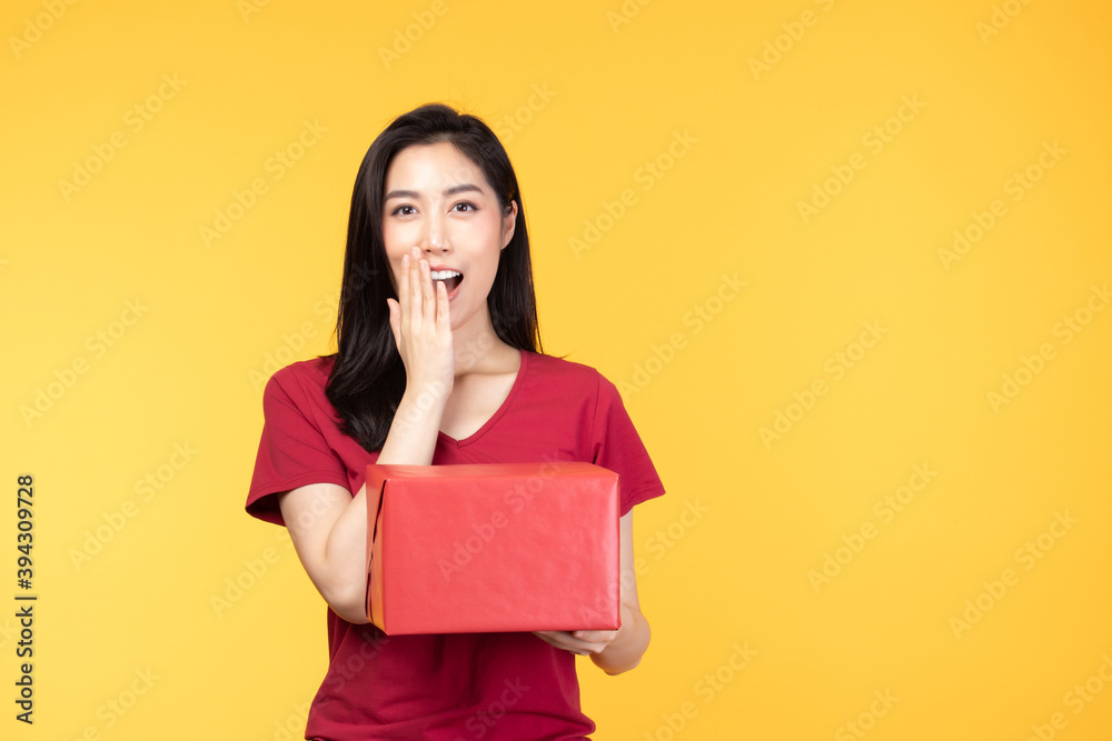 Portrait of happy smiling girl in casual holding gift box and expression face isolated over yellow background Portrait of happy smiling girl in casual holding gift box and expression face isolated over yellow background