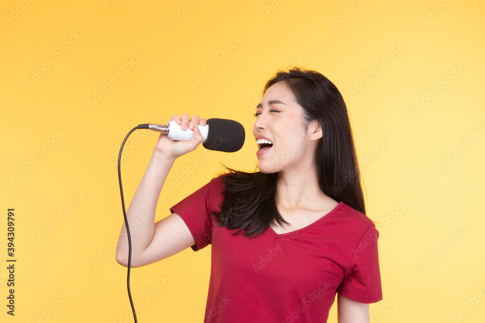 Pretty Asian woman in casual wear holding microphone and singing on yellow background. Pretty Asian woman in casual wear holding microphone and singing on yellow background.