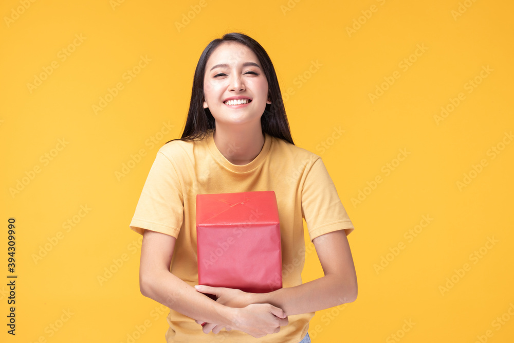 Portrait of happy smiling girl in casual holding gift box and expression face isolated over yellow background Portrait of happy smiling girl in casual holding gift box and expression face isolated over yellow background