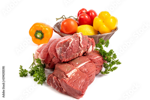 Two pieces of beef sirloin tip roast with a basket of peppers, onions, lemon and tomatoes isolated on white 