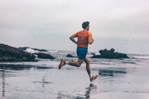 Exercise outdoor athlete man running on wet sand at beach training cardio sprinting fast. Profile of runner in sportswear clothes jogging.