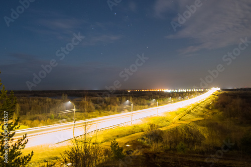 the road, brightly lit by street lamps, goes beyond the horizon against the background of the starry sky