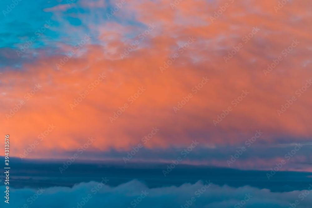 View of colorful fluffy clouds from an airplane at sunset, orange and teal cloudscape treatment