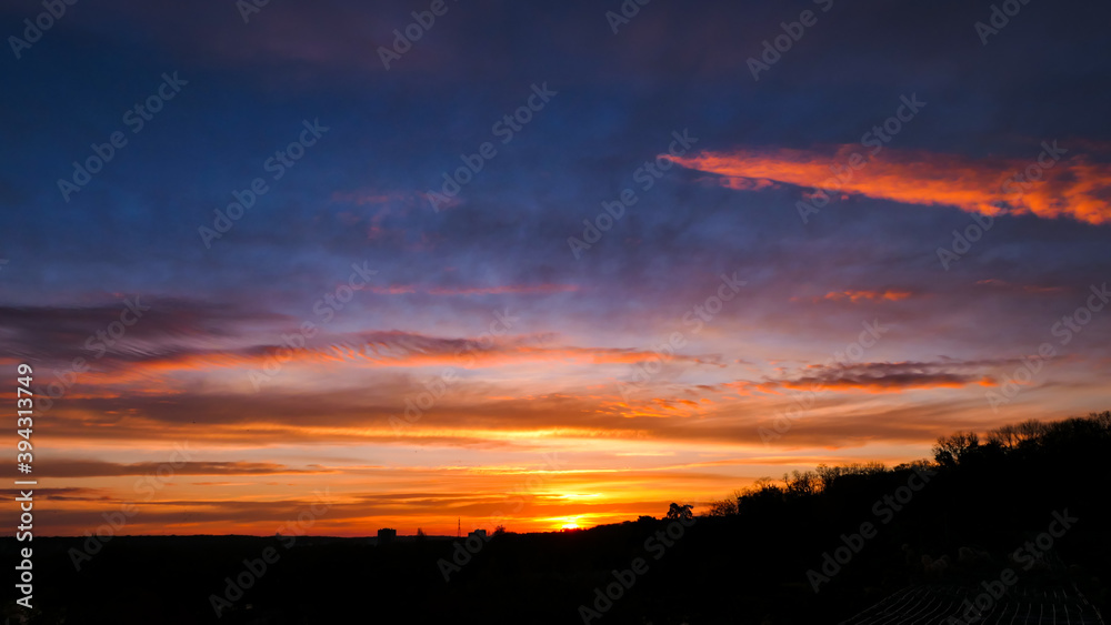 Fototapeta premium Amazing sunrise in rural scene. Dramatic sky with sunbeam and stratus clouds over the silhouette of hill on the horizon.