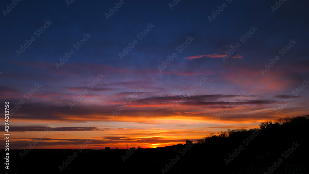 Obraz premium Amazing sunrise in rural scene. Dramatic sky with sunbeam and stratus clouds over the silhouette of hill on the horizon.