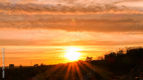 Amazing sunrise in rural scene. Dramatic sky with sunbeam and stratus clouds over the silhouette of hill on the horizon.