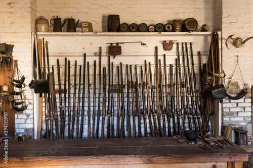 Tall rack of black powder rifles against a brick wall inside a fort armory photo