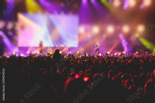 A crowded concert hall with scene stage lights, rock show performance, with people silhouette, colourful confetti explosion fired on dance floor air during a concert festival