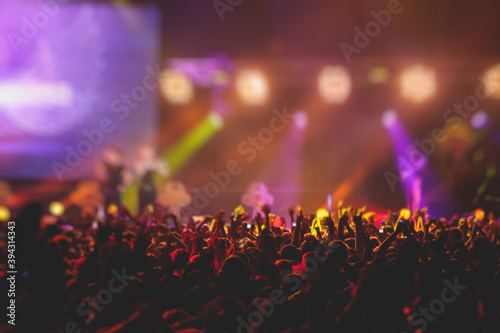 A crowded concert hall with scene stage lights, rock show performance, with people silhouette, colourful confetti explosion fired on dance floor air during a concert festival