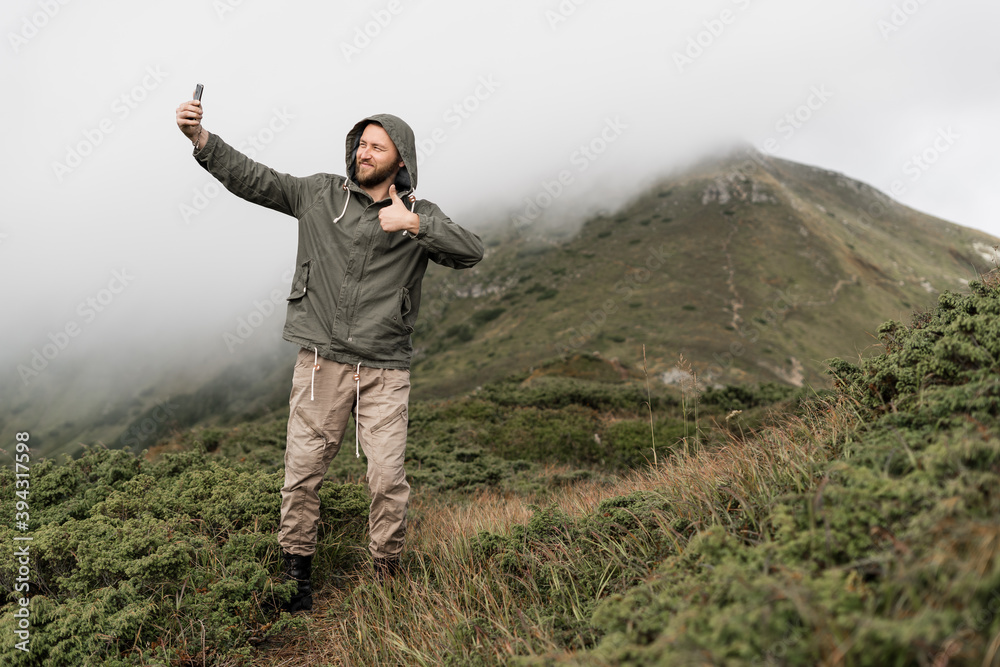 Young traveler stands on the top of the mountain and takes a photo on a smartphone from behind. Place for text. Tourism concept.