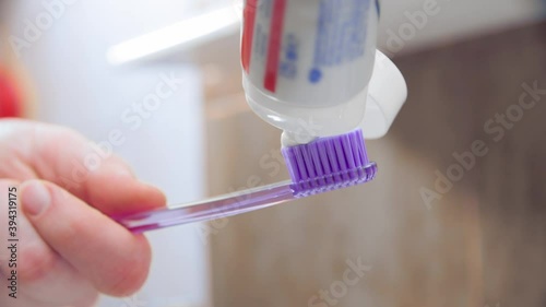 Female hand squeezing tooth paste on blue toothbrush in bathroom
