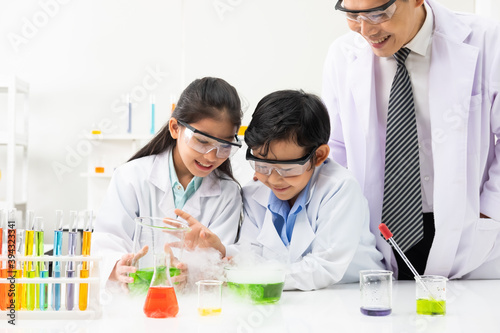 Young Asian boy and girl student wearing protective google while study and do science experiment in classroom with teacher. Learning and having fun moment. Chemist or biology classroom concept.