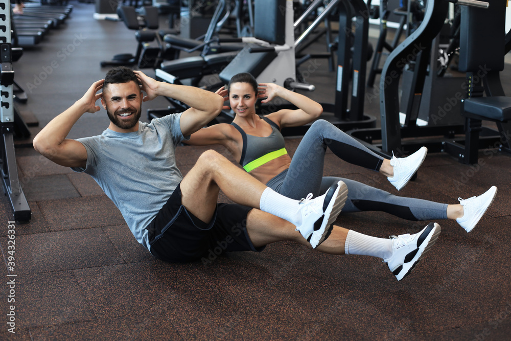 Attractive man and woman working in pairs performing sit ups in gym. Attractive man and woman working in pairs performing sit ups in gym.