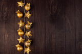 Elegant christmas golden decoration with warm stars lights garland  on dark brown wood board, top view, copy space, New Year background.