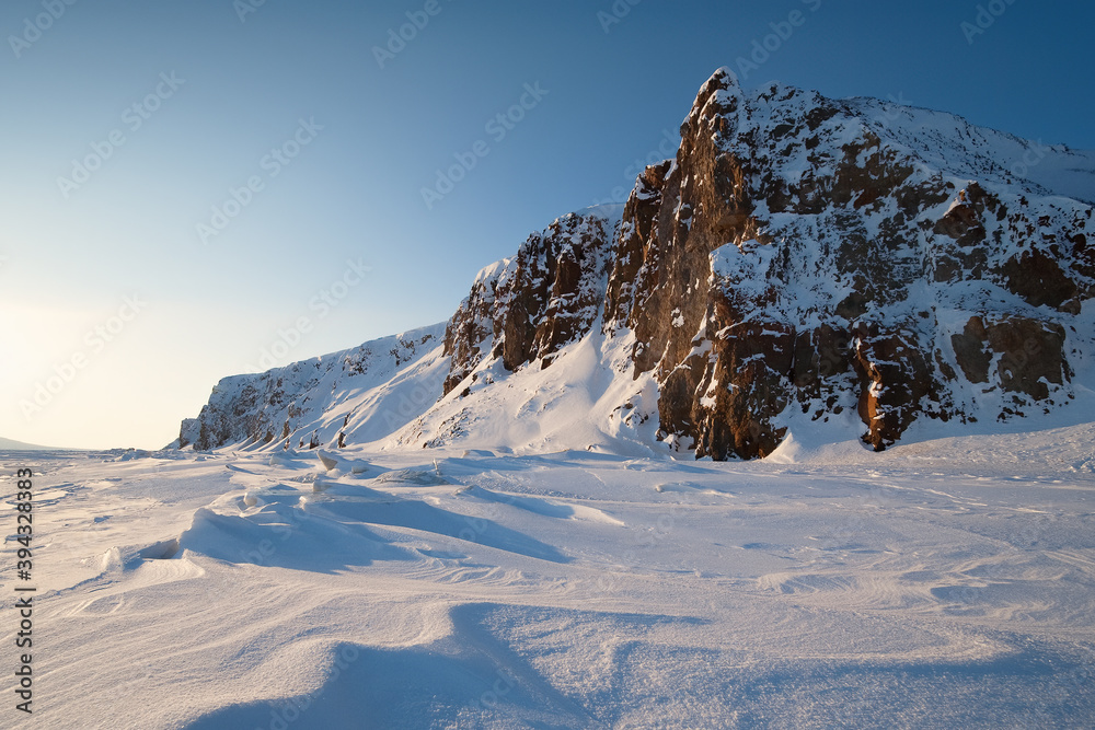 Winter arctic landscape. View of the rocky coast of the frozen sea. Nature of the Arctic and polar Siberia. Cold frosty winter weather. Snow-capped rocks and a high cliff. Chukotka, Far East Russia.