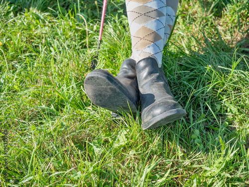 Young girl in paddock boots with long tighs sitting in meadow and waiting for her horse and riding lesson. photo