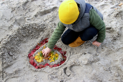 A child draws a heart in the sand.  © Galina