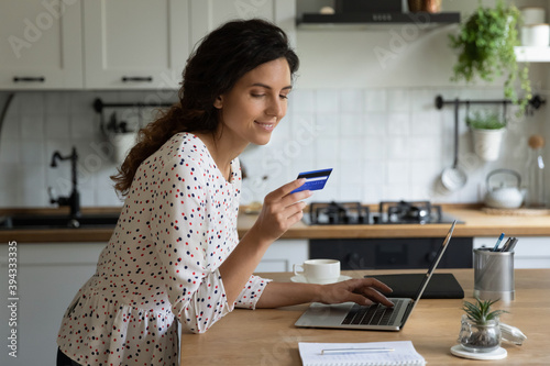 Smiling Caucasian female buyer shopping online on computer from home pay with credit card. Happy young woman client make payment or purchase, place order on internet, use secure banking system.