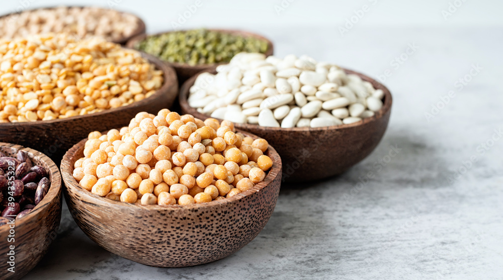 Various dried legumes in wooden bowls on white marble background