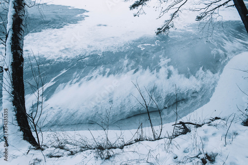 Cracks on the surface of the blue ice. Frozen lake in winter mountains. It is snowing. The hills of pines. Russian Sibirea photo