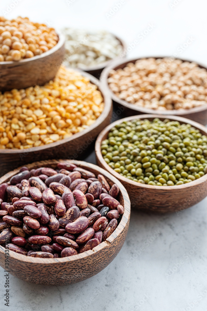 Various dried legumes in wooden bowls on white marble background Various dried legumes in wooden bowls on white marble background