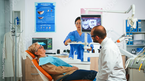Man dentistry doctor pointing on digital screen showing dental implants. Dentist and nurse working together in modern stomatological clinic  explaining radiography of teeth on monitor