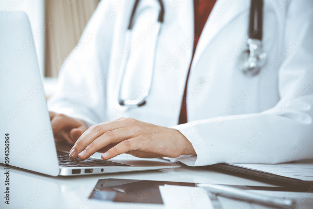 Unknown woman-doctor typing on laptop computer while sitting at the table. Medicine concept Unknown woman-doctor typing on laptop computer while sitting at the table. Medicine concept