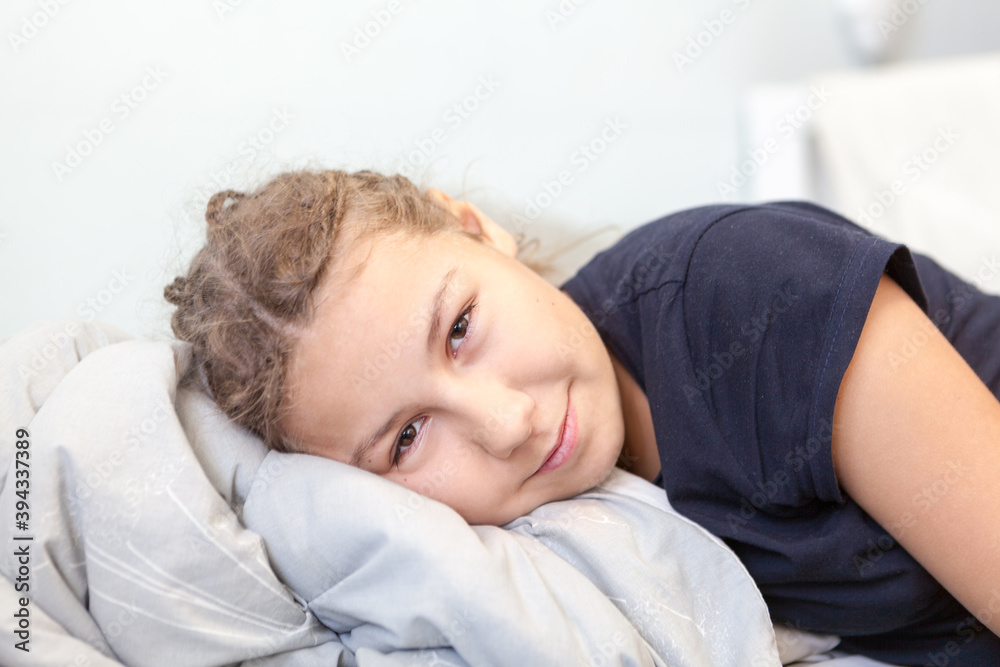 Beautiful teen girl lying with comfortable pillow on bed, looking at camera