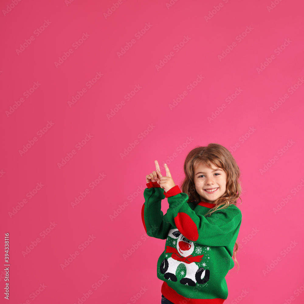 Cute little girl in green Christmas sweater pointing against pink background. Space for text Cute little girl in green Christmas sweater pointing against pink background. Space for text