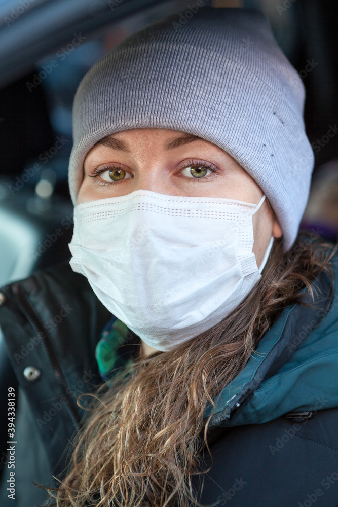 Curly hair Caucasian woman in safety mask sitting inside her car, female wearing hat and coat