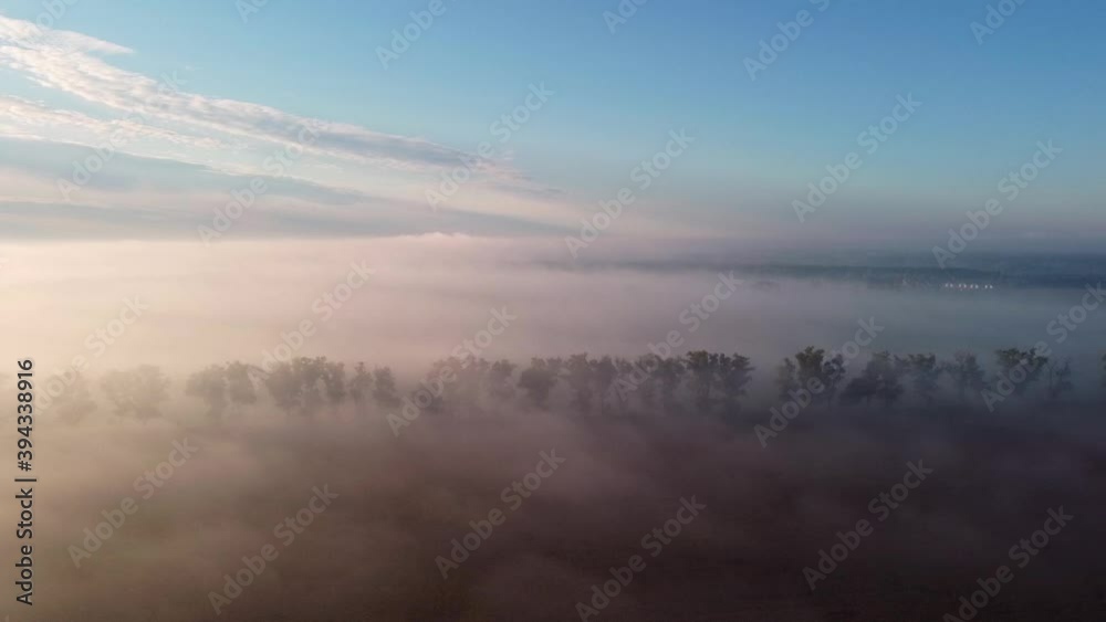 Countryside landscape shrouded in a thick blanket of fog illuminated by the warm light of the rising sun. Aerial pan from right to left. Countryside landscape shrouded in a thick blanket of fog illuminated by the warm light of the rising sun. Aerial pan from right to left.