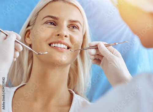 Smiling blonde woman examined by dentist at sunny dental clinic. Healthy teeth and medicine concept