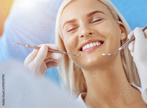 Smiling blonde woman examined by dentist at sunny dental clinic. Healthy teeth and medicine concept