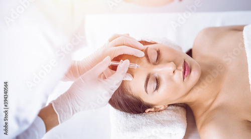 Beautician doing beauty procedure with syringe to face of young brunette woman in sunny spa center. Cosmetic medicine and surgery, beauty injections