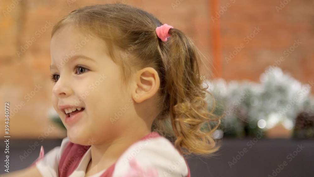 Portrait of a little smiling girl close-up. Cute three year old girl with ponytails smiling at someone off-screen. Joyful child smiles with open mouth with white teeth. Portrait of a little smiling girl close-up. Cute three year old girl with ponytails smiling at someone off-screen. Joyful child smiles with open mouth with white teeth.