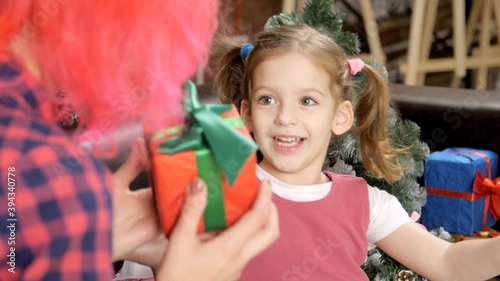 Modern mom with red hair gives a gift box to her little smiling daughter. Three-year-old beautiful girl laughs and rejoices at the Christmas or New Year gift. Positive emotions  happy child. 